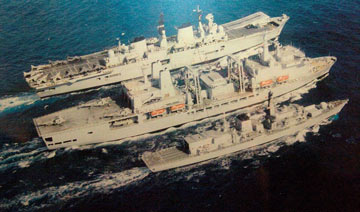 merchant ship alongside two large Royal Navy ships at sea