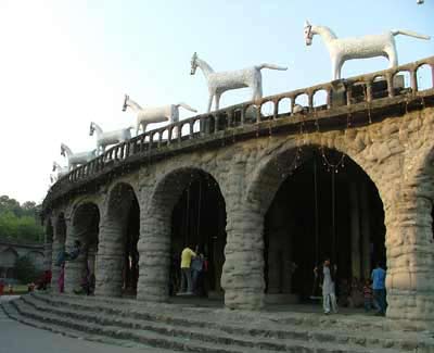 A series of arch ways, which each have a swing attached, many of the swings have people using them. Above the arches stand a series of enormous horses decorated with white mosaic