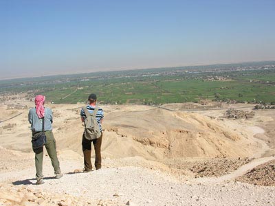Two men on a barren hill looking down to a lush river valley