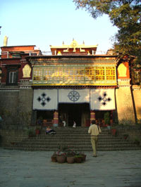 A pale brick built building with steps leading up the entrance. Its pagaoda style roof is decorated with gilt Tibetan Buddhist embelms
