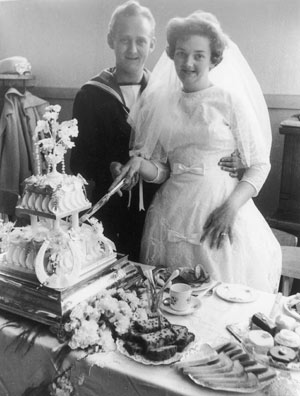 man in sailor's uniform and woman in wedding dress cutting their wedding cake