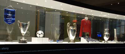 a glass cabinet containing four large silver trophies and several football shirts