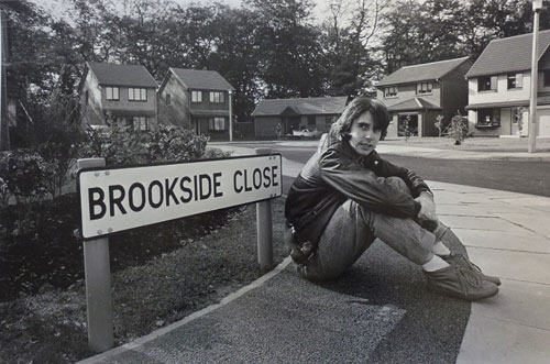 Phil Redmond sitting by a 'Brookside Close' street sign