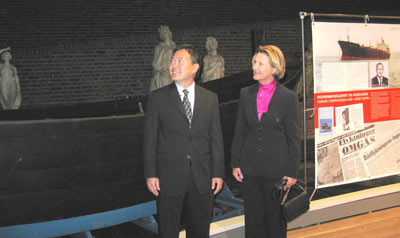 smartly dressed man and woman standing next to a wooden boat in a museum display