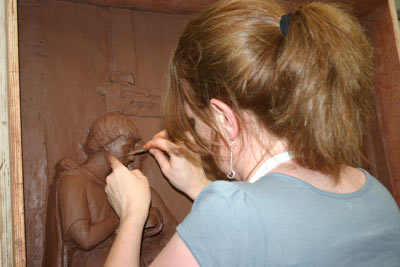 woman sculpting a clay figure on a relief sculpture