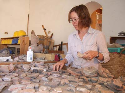 woman examining lots of pieces of ancient pottery on a table
