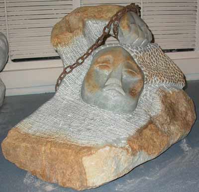 large rock of pale stone, carved with human face and arm, and a rusted chain wrapped around the wrist