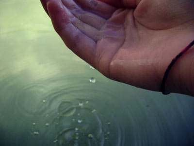 photo of water dripping from a hand creating ripples in water below