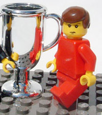 a photo of a lego man in red standing next to a lego trophy