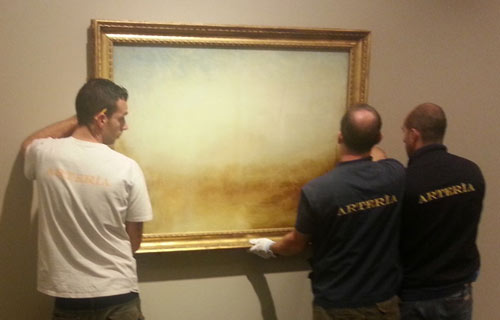 men wearing white gloves hanging a painting on a wall