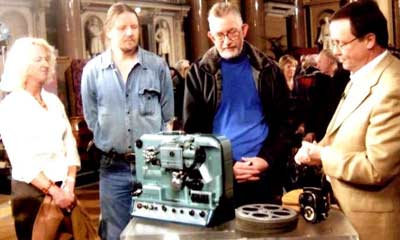 photo of four people standing around a old projector and a stack of old film