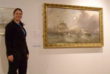 woman standing by a painting of sailing ships in a rough sea