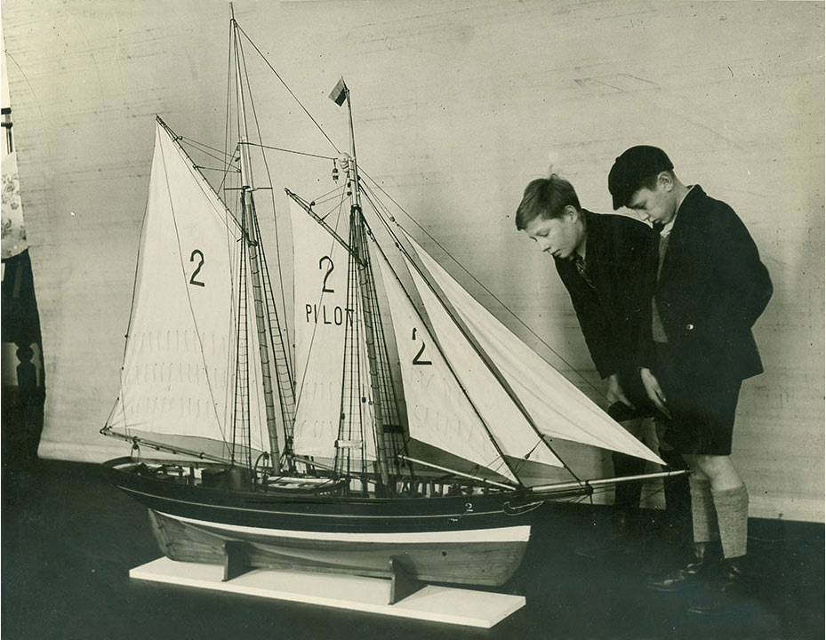 boys in school uniform looking at a sailing ship model that's almost as tall as them