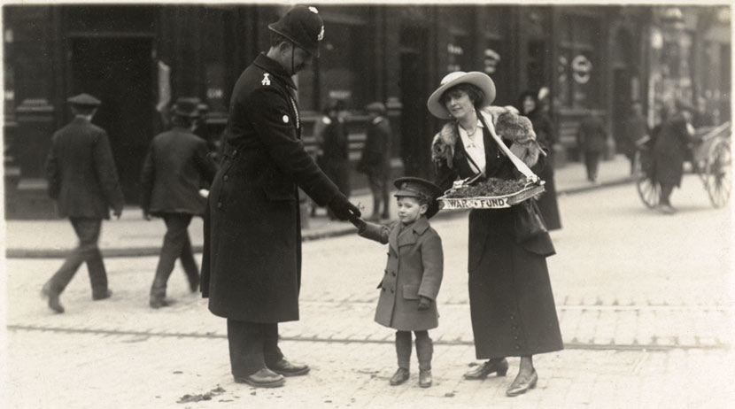 A small boy dressed in uniform sells charity flowers to a policeman