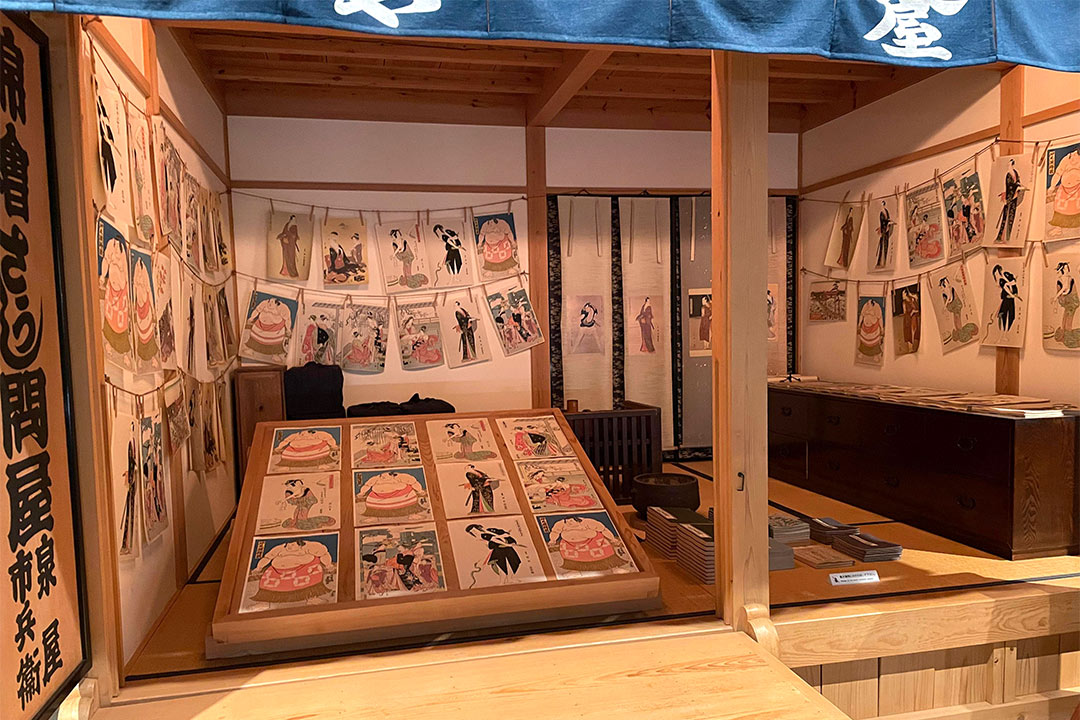 model of a print shop with many Japanese prints on tables and hanging round the walls