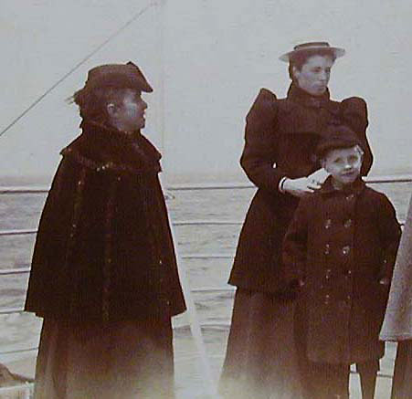 Two women and a boy, all smartly dressed, by the railings on the deck of a ship
