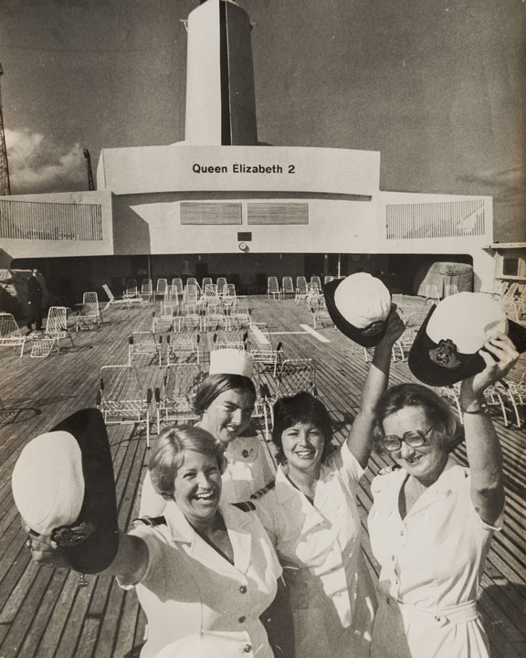 women in uniform raising their hats on the deck of the QE2 cruise liner