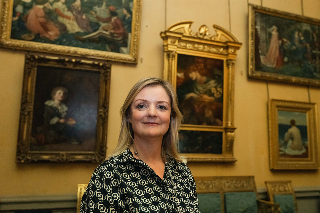 Rebecca in front of Victorian paintings with elaborate gold frames