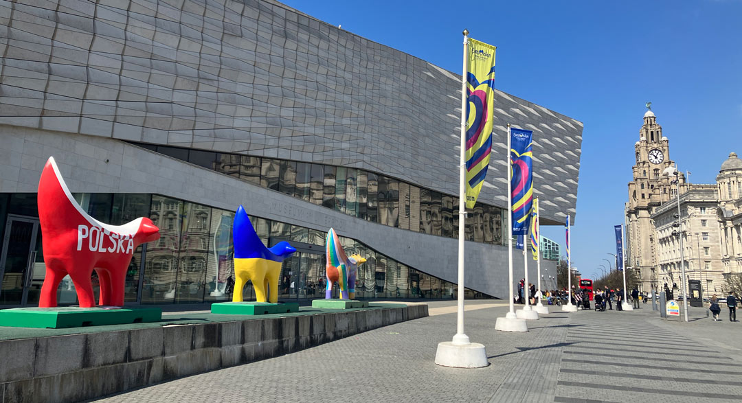 colourful sculptures in the shape of lambs with banana tails outside the Museum of Liverpool with the Liver Building in the background