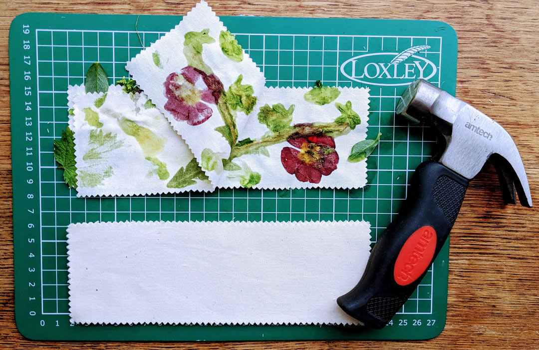 fabric strip peeled back to show the colours of the flower and leaves beneath printed onto it, next to hammer on a cutting board