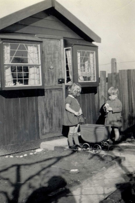 two small children by a large shed-like Wendy house