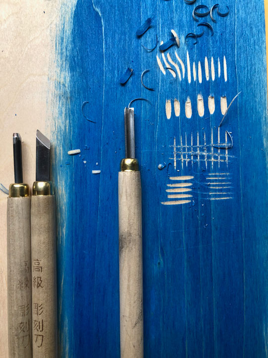 wood carving tools, with practice marks cut into inked up wooden block